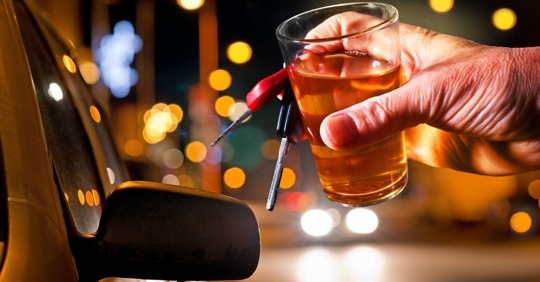 Man with a glass of alcohol and keys in his hand reaching for a car.